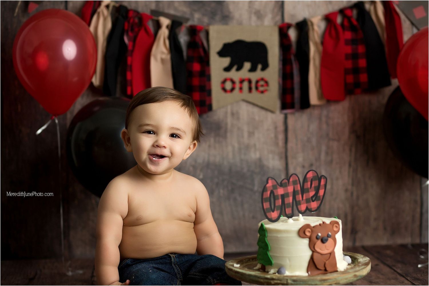 A festive first birthday party setup with buffalo plaid decorations, red balloons, and woodland animal theme.