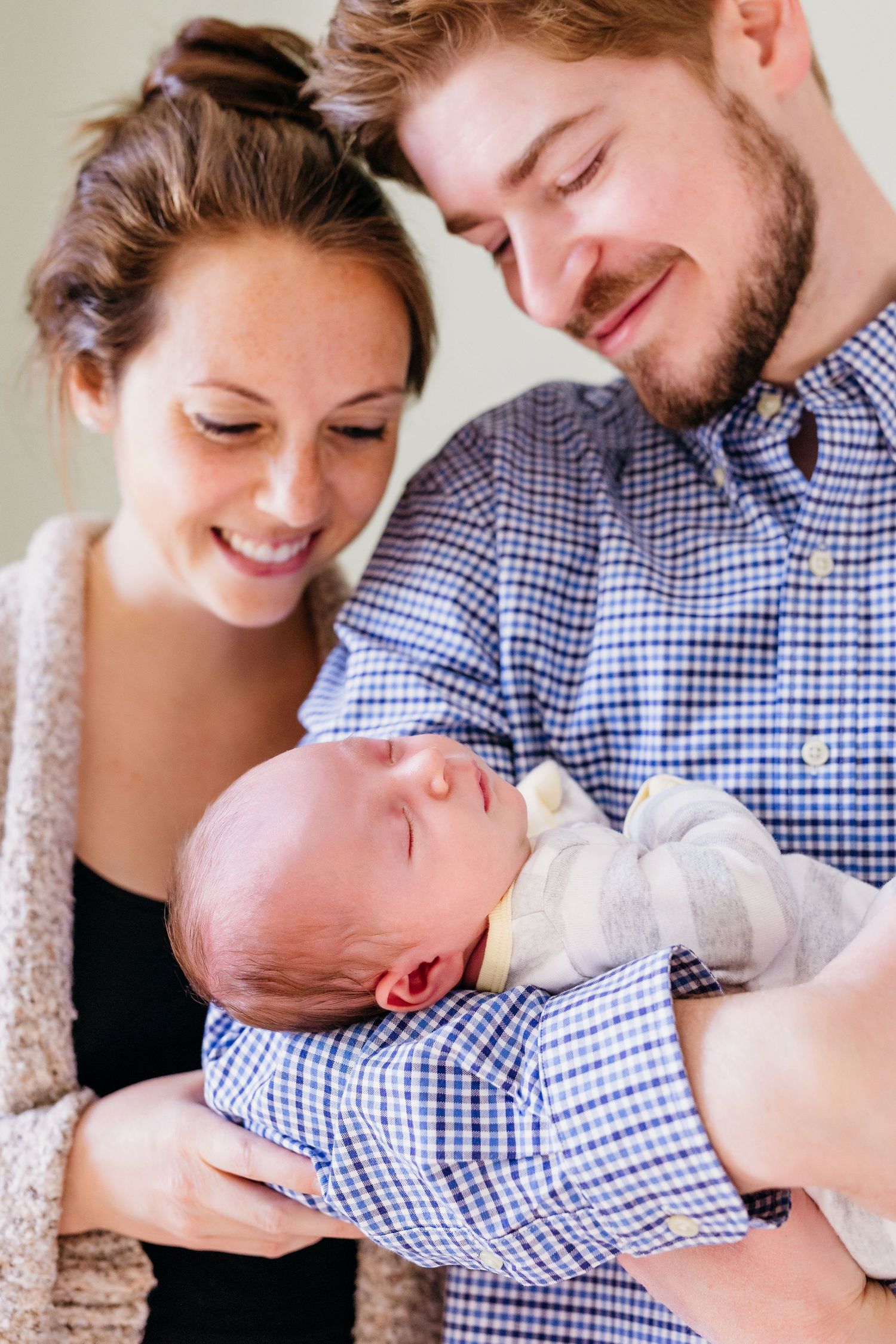 Intimate family moment captured in soft natural light with newborn baby on white bedding.