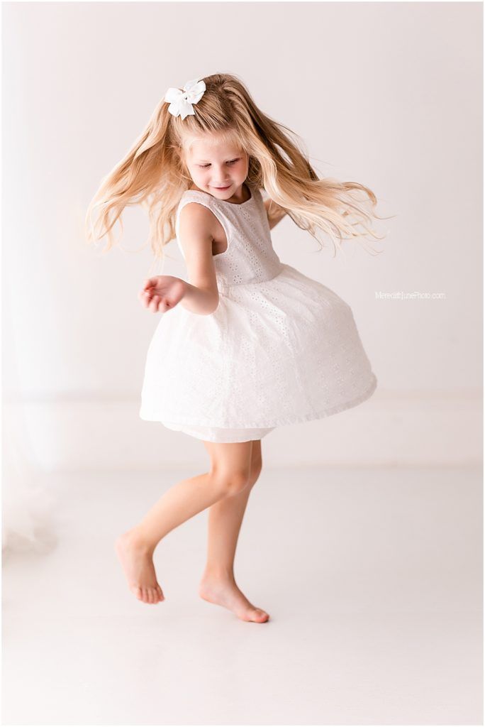 A young dancer in a white dress twirls and spins across a bright studio space in a graceful sequence.
