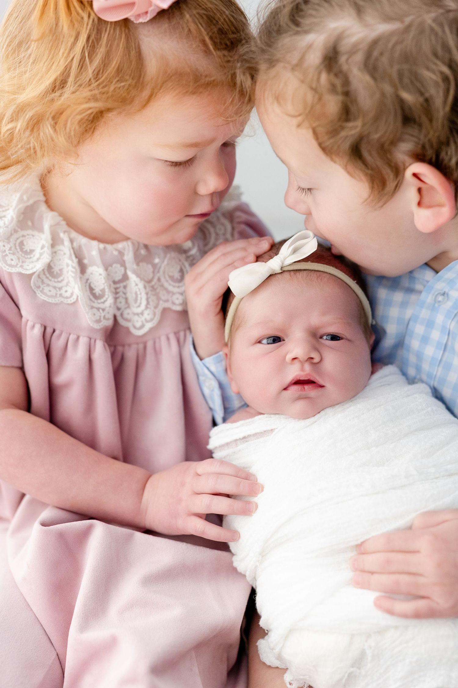 Three heartwarming photos showing siblings bonding with a newborn baby in soft pink and white tones.