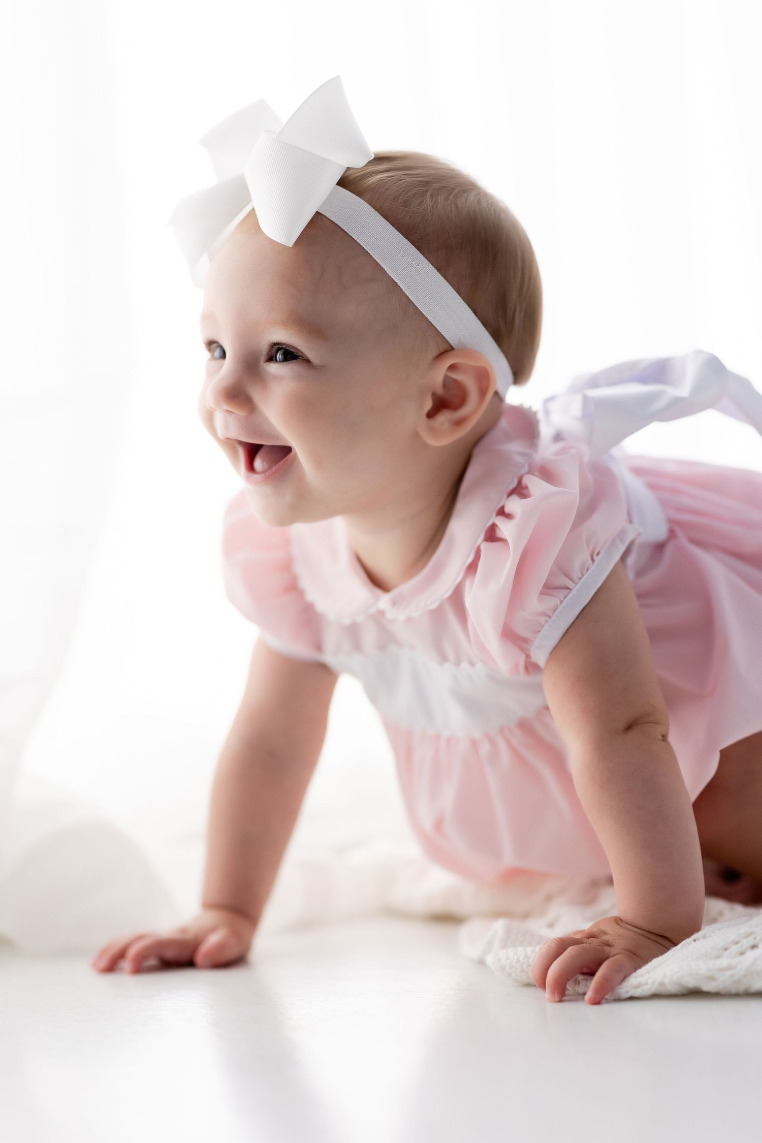 Baby in pink dress crawls and plays on white background in sequence of photos.
