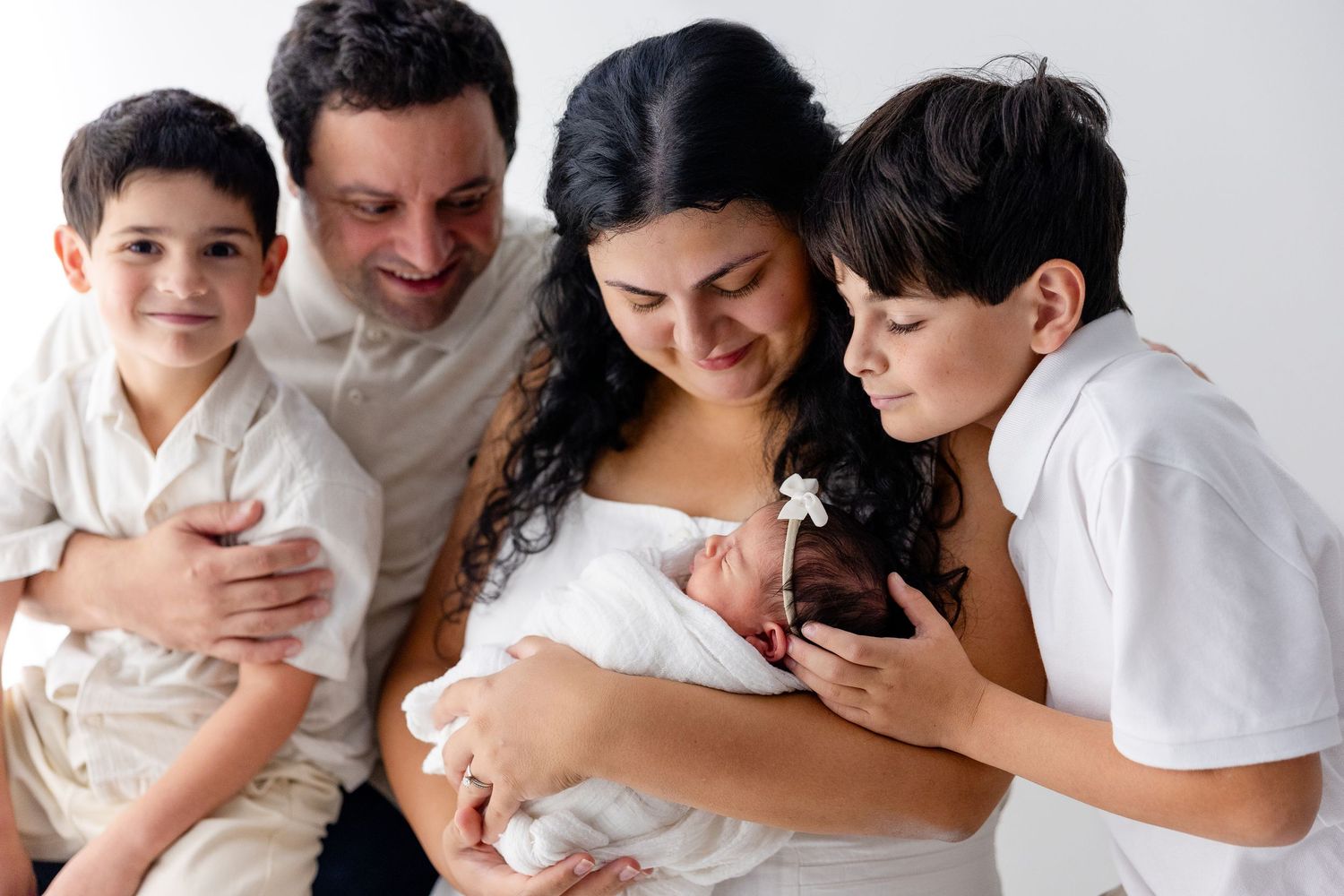 Family portrait series in white showing tender moments with their newborn.