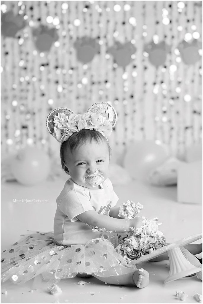 Black and white photo of baby in tulle skirt with sparkly decorations and string lights in background.