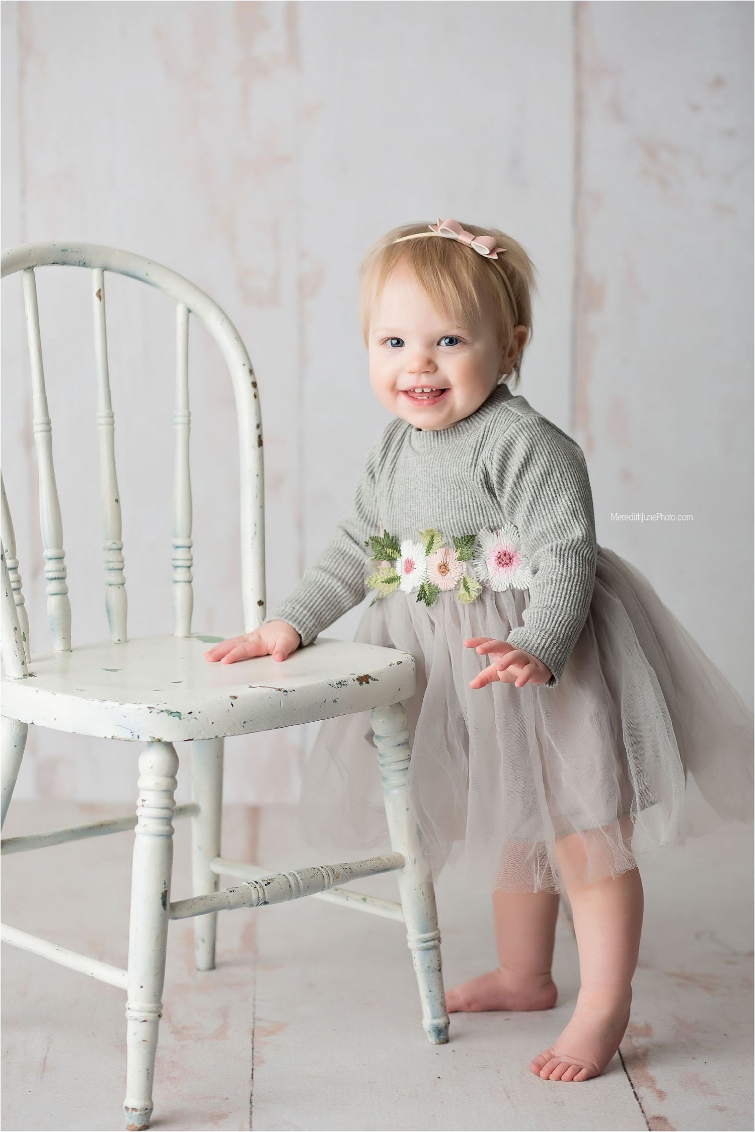 A series of photos showing a small child in a gray sweater and tulle skirt exploring a vintage white wooden chair.