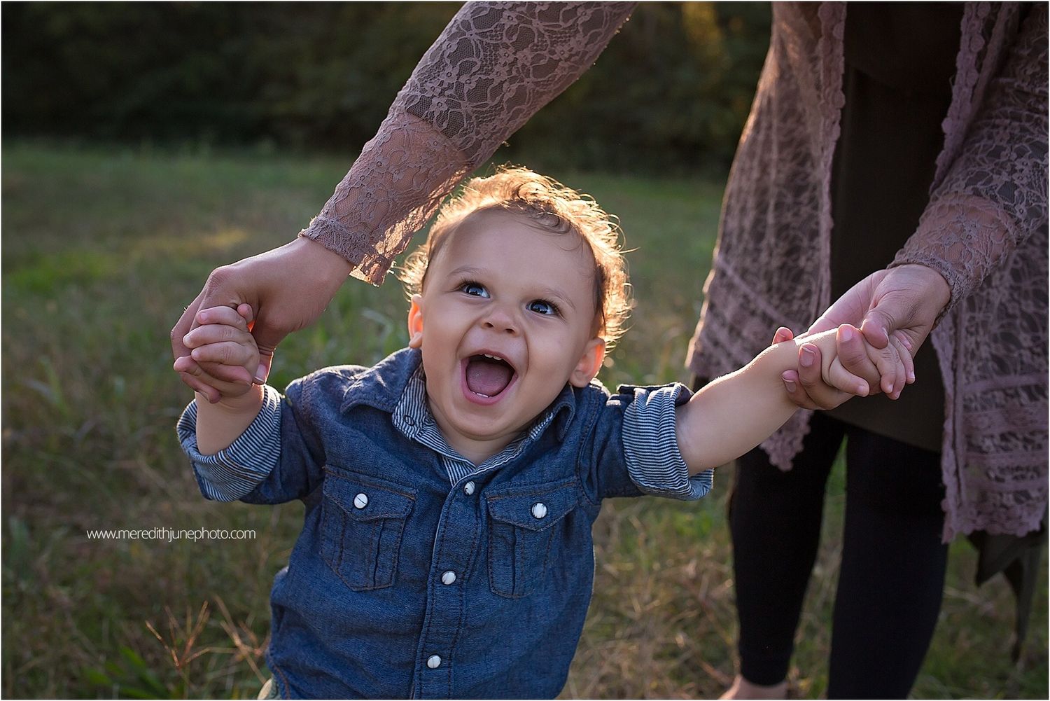 Child laughing and playing while being held up in a grassy field at sunset.
