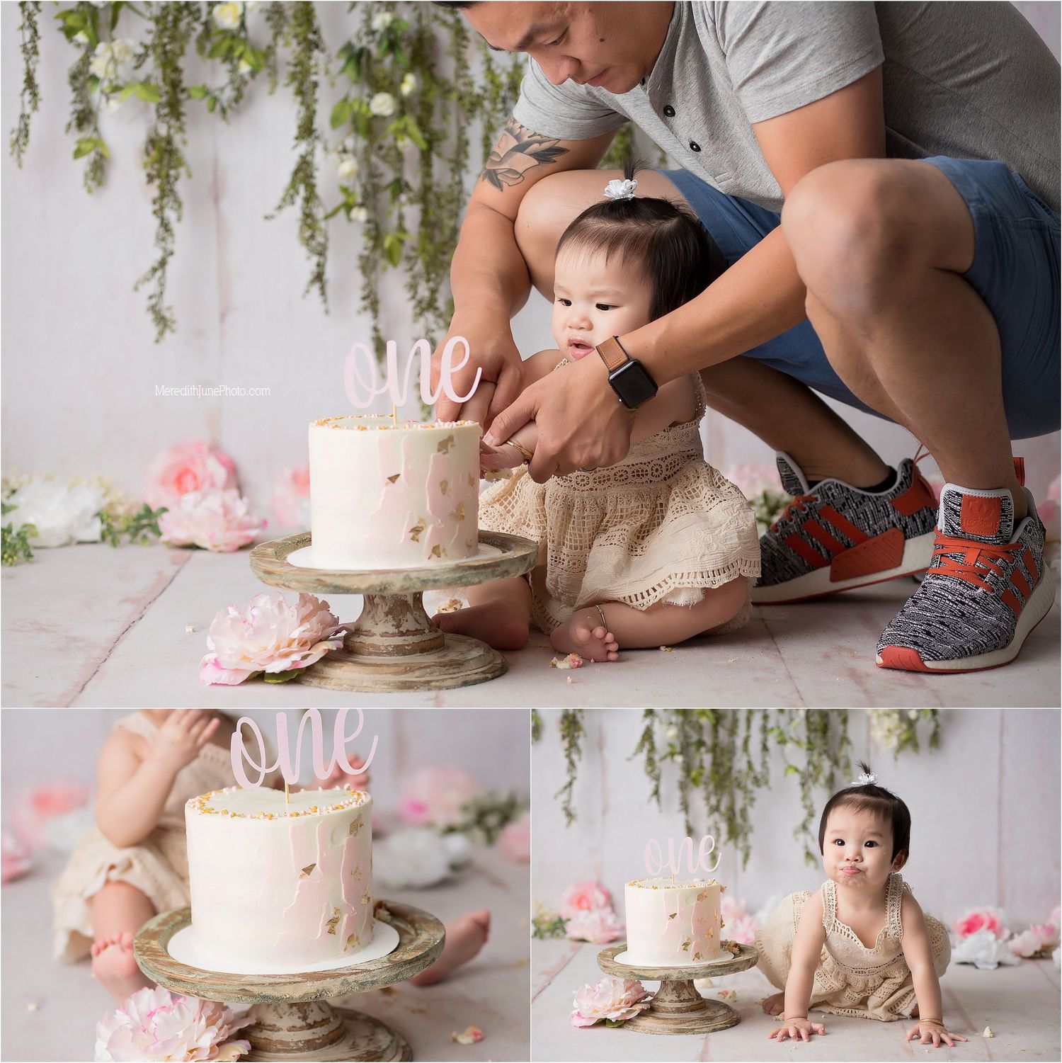 Baby in white outfit sits on floor while someone decorates a pink and white birthday cake during cake smash photo session.