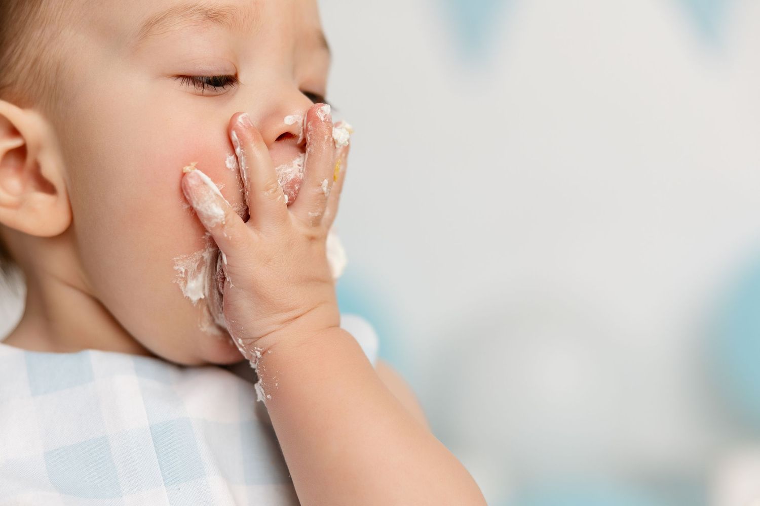A young child holds a finger to their lips in a shushing gesture against a bright background.