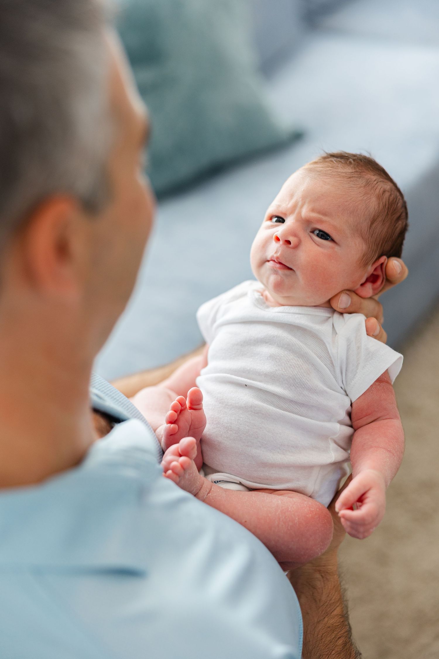 A newborn baby wearing a white onesie is being gently held and examined.