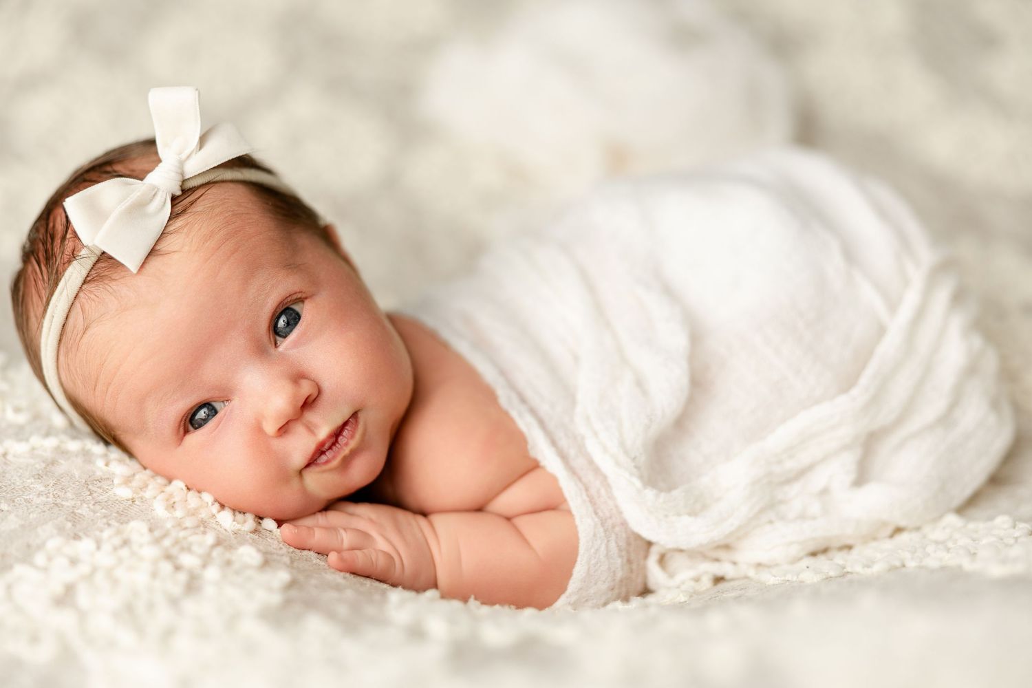 A baby lies swaddled in soft white blankets, creating a gentle and peaceful newborn portrait.