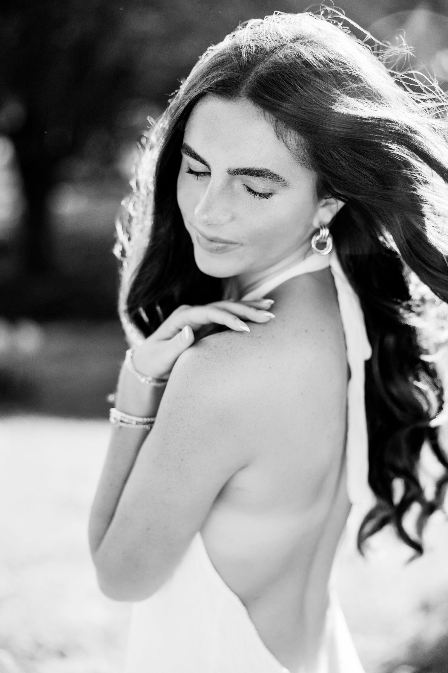 Black and white portrait of a young woman with long wavy hair, wearing drop earrings, glancing down gracefully.
