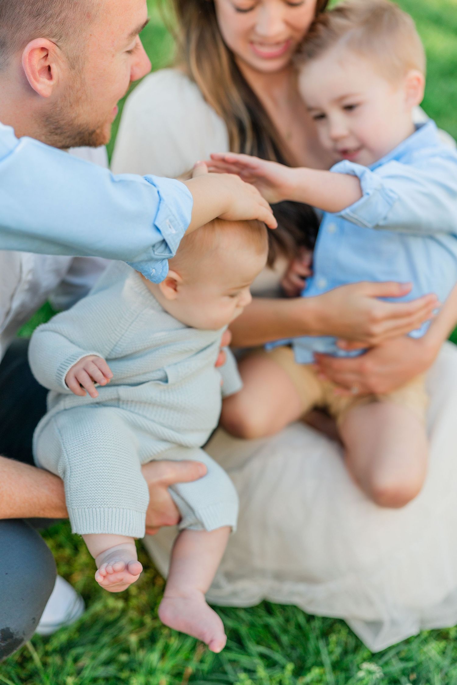 A family shares tender moments while sitting together on grass in soft afternoon light.
