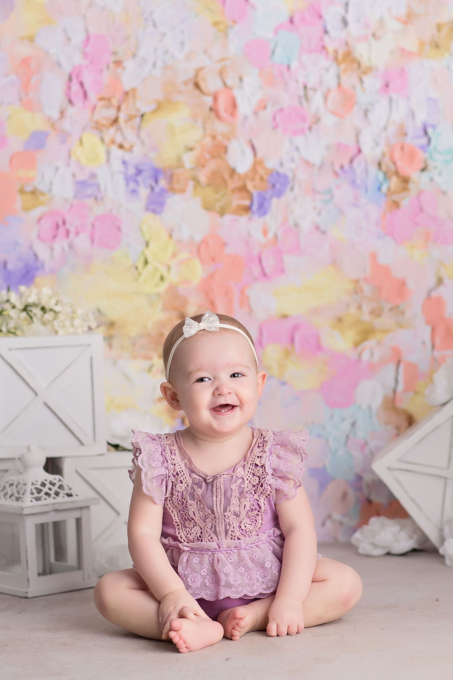 Colorful pastel backdrop with white decorative lanterns creates a whimsical setting for a baby photography session.
