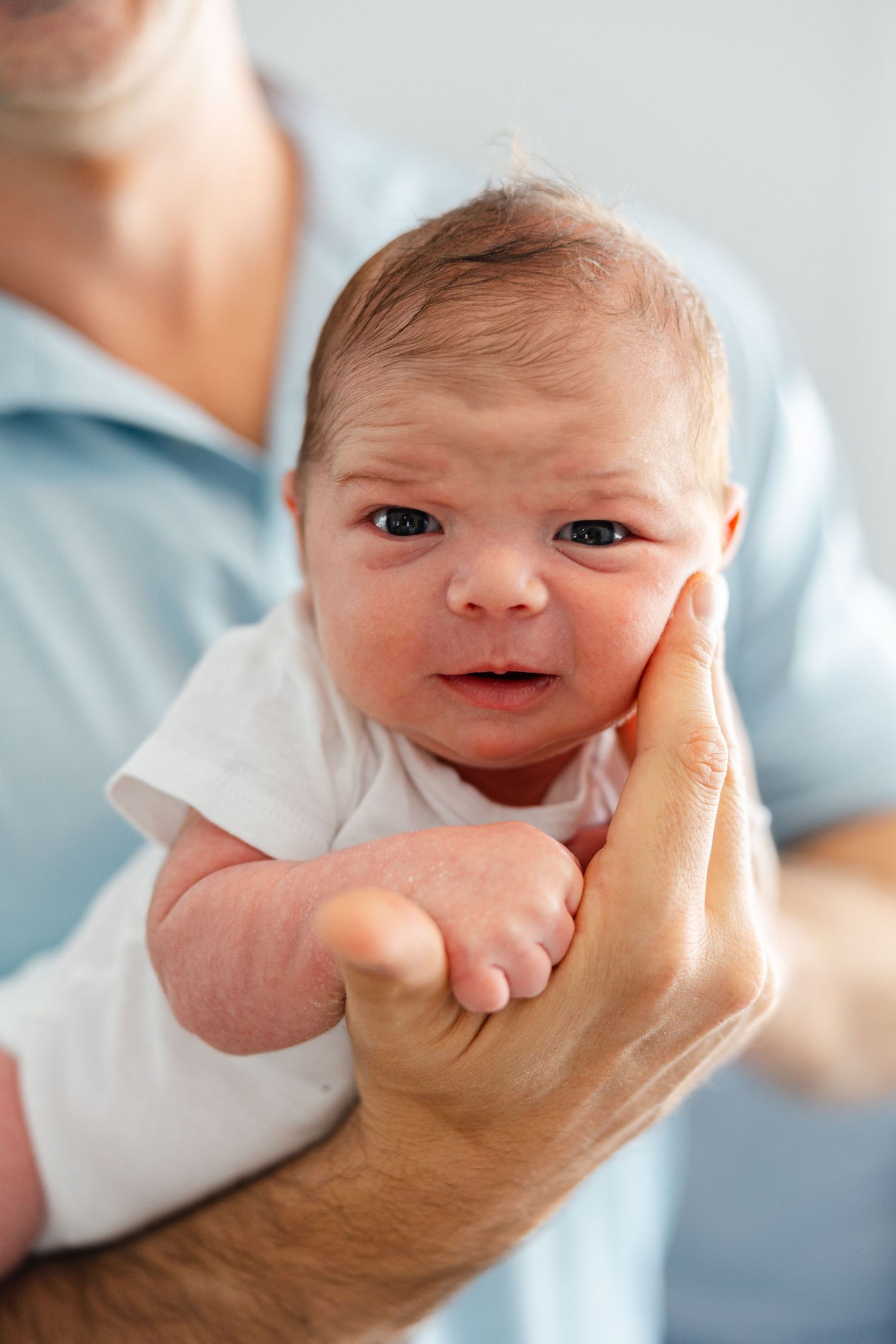 A series of photos showing a newborn baby's expressive faces as gentle hands cradle their head in soft lighting.