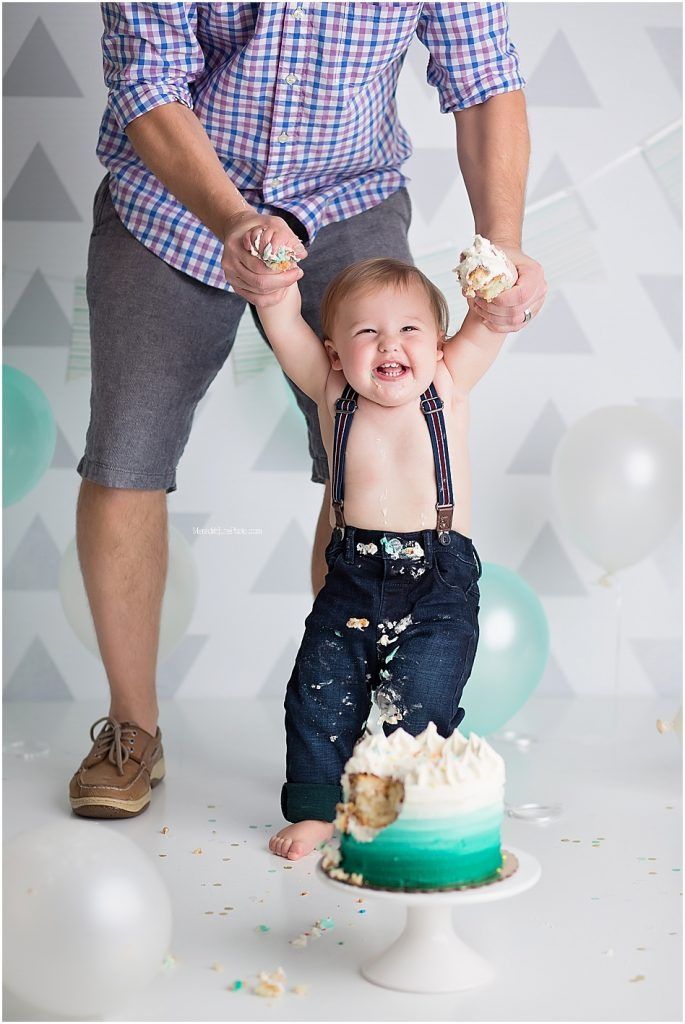First birthday cake smash session with baby in overalls getting messy with teal and white cake.