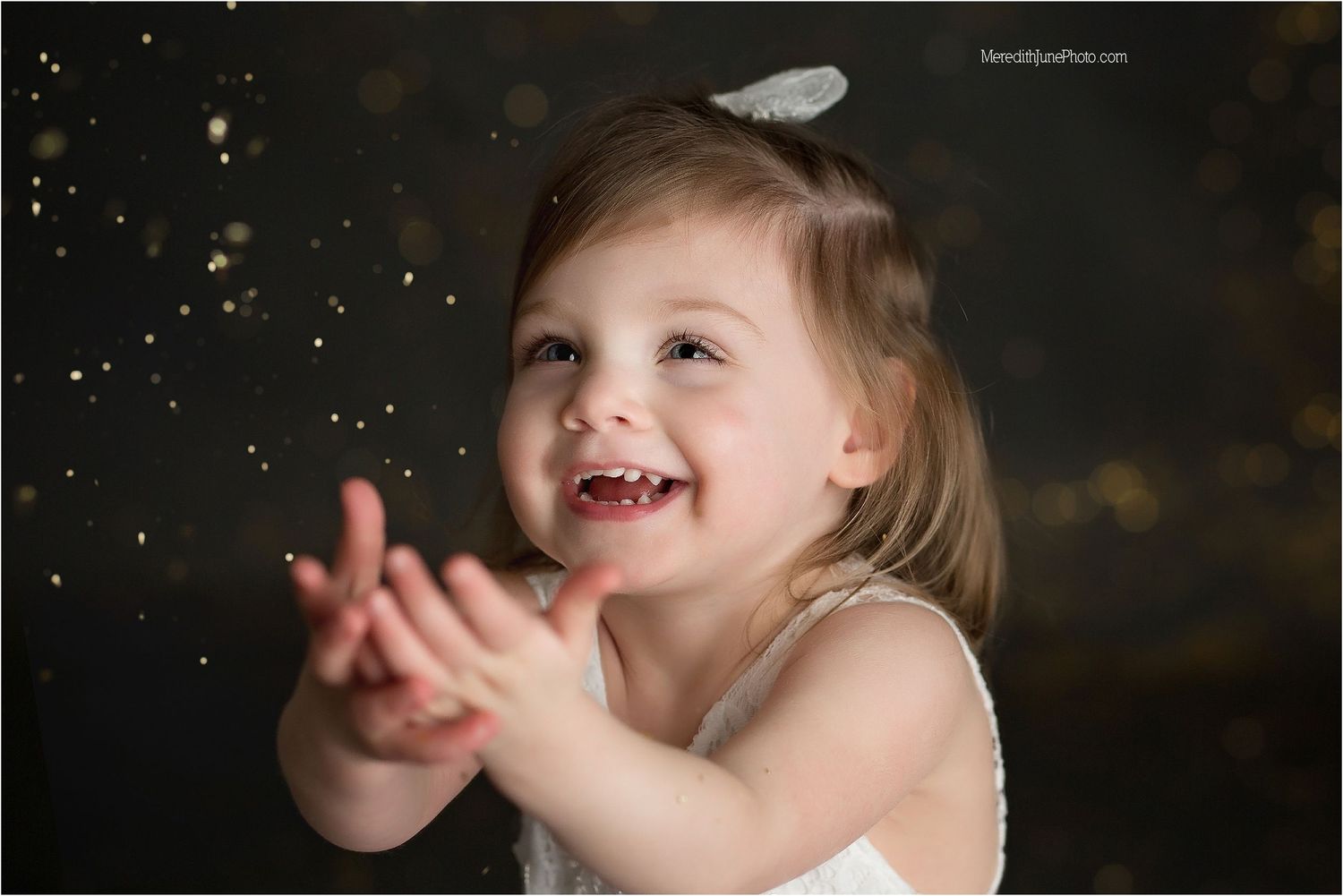 Child plays with falling glitter during magical portrait session with dark background.