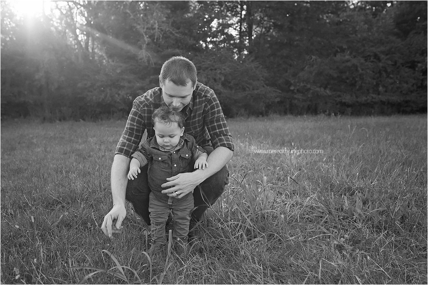 A tender moment captured in black and white as parent and child explore a sunlit meadow together.