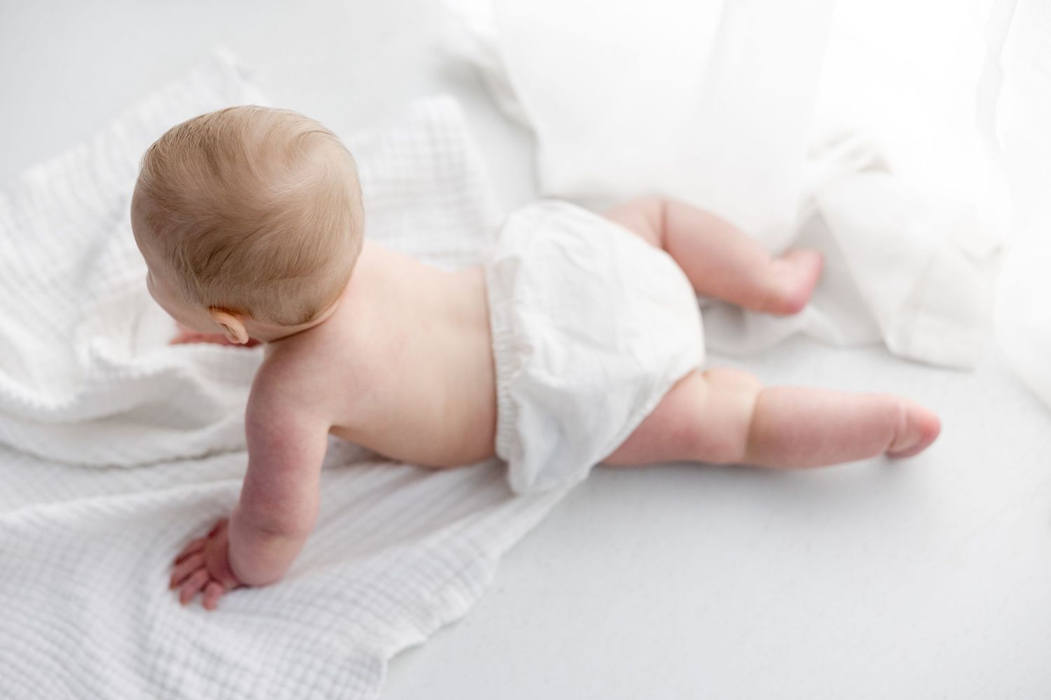 Newborn baby wrapped in white fabric lying on soft blankets in a series of artistic poses.