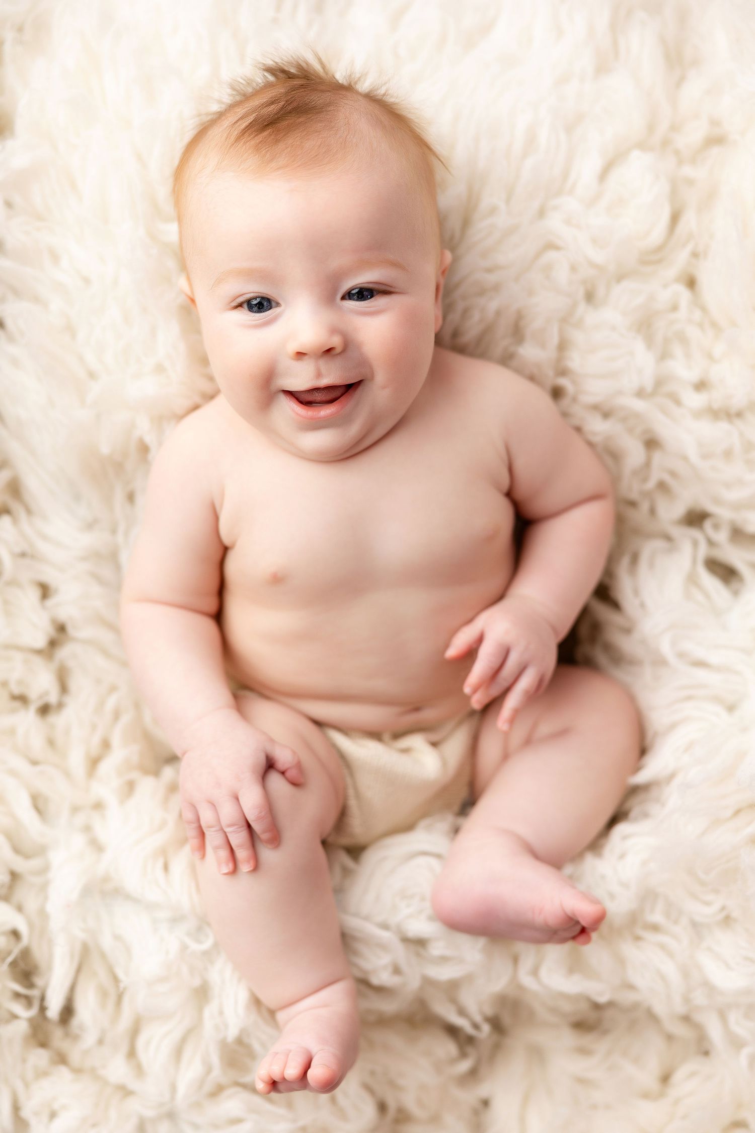 Smiling baby lying on soft cream-colored textured blanket in natural light.