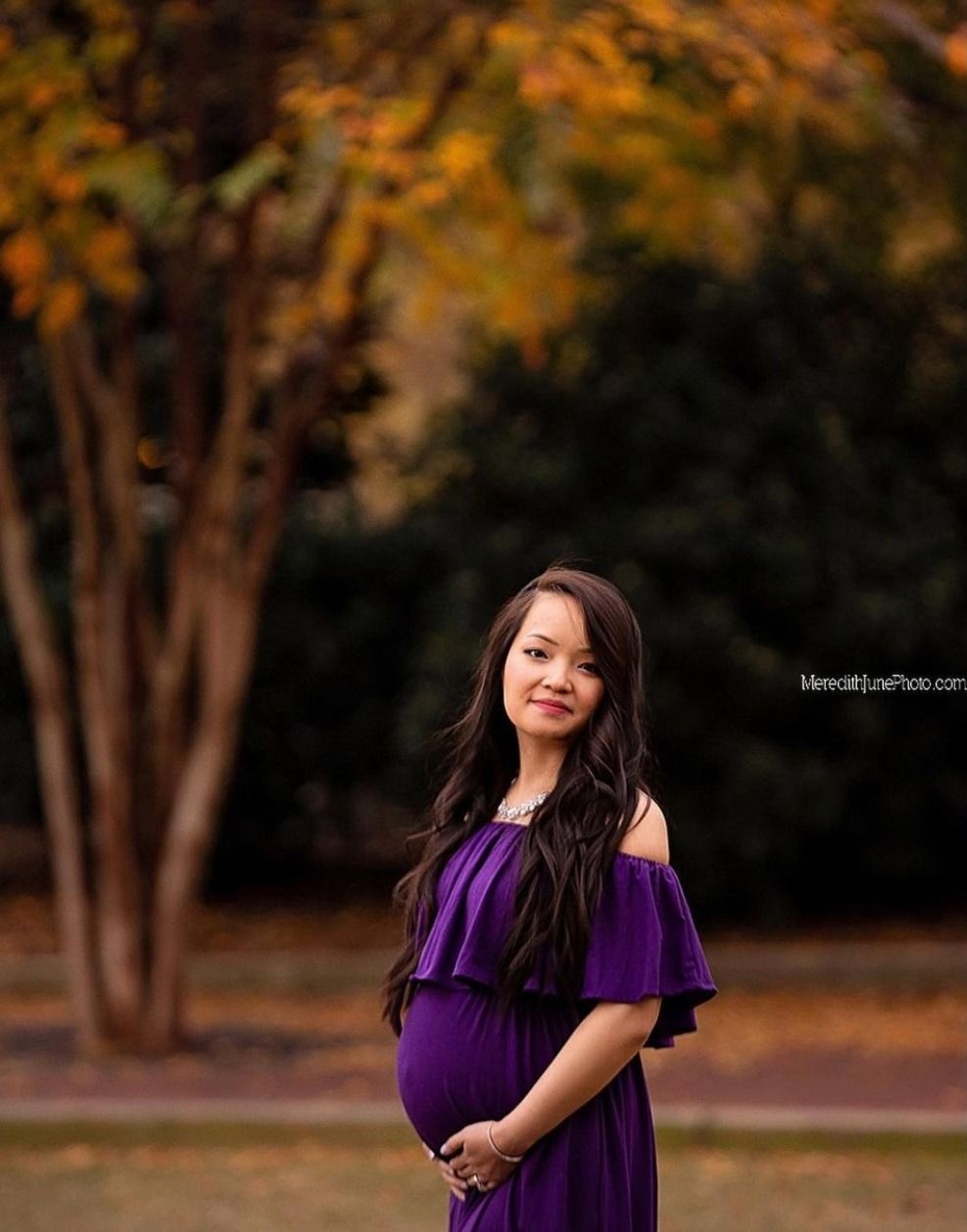 A maternity photoshoot featuring a purple dress against warm autumn foliage.