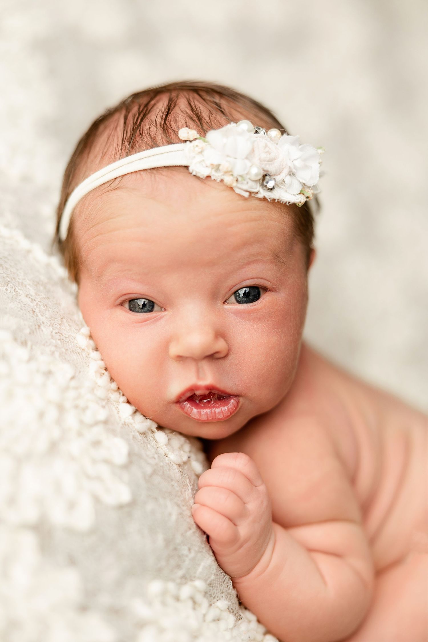Newborn baby wearing lace headband on soft white backdrop.