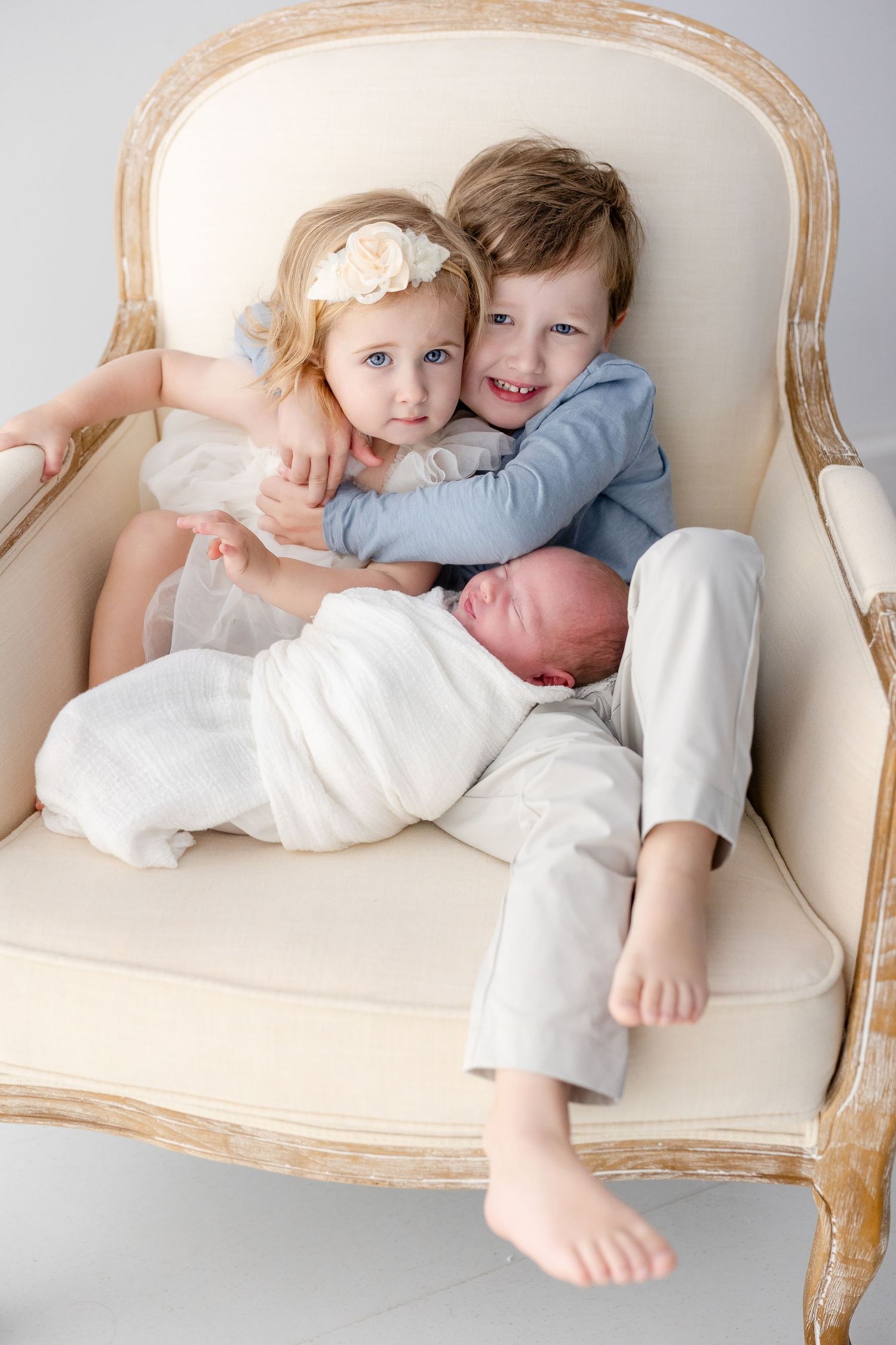 Children in white outfits play and cuddle together on an elegant cream-colored settee.