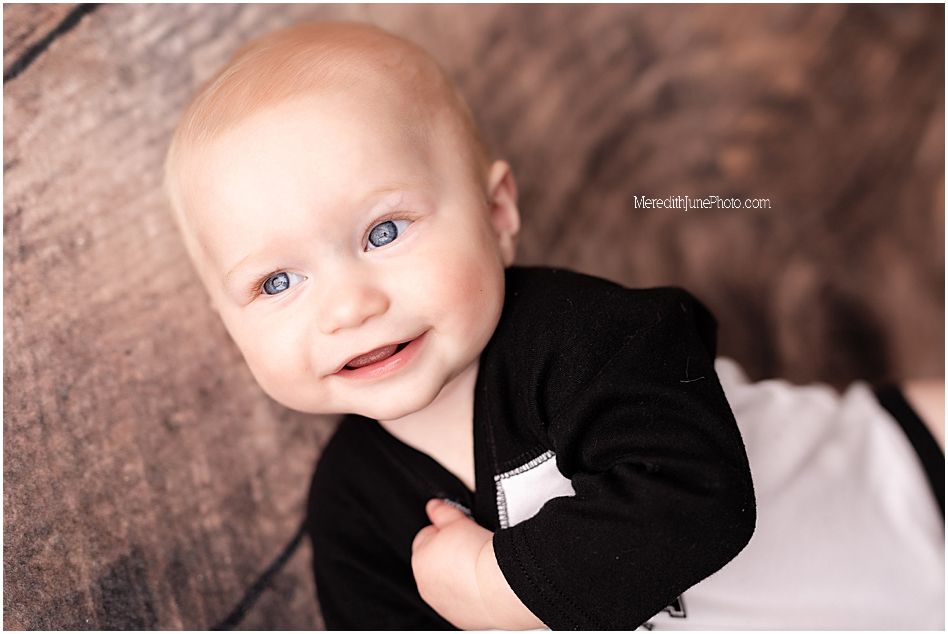 A baby wearing a black shirt smiles while lying on a white background in a professional photo shoot.