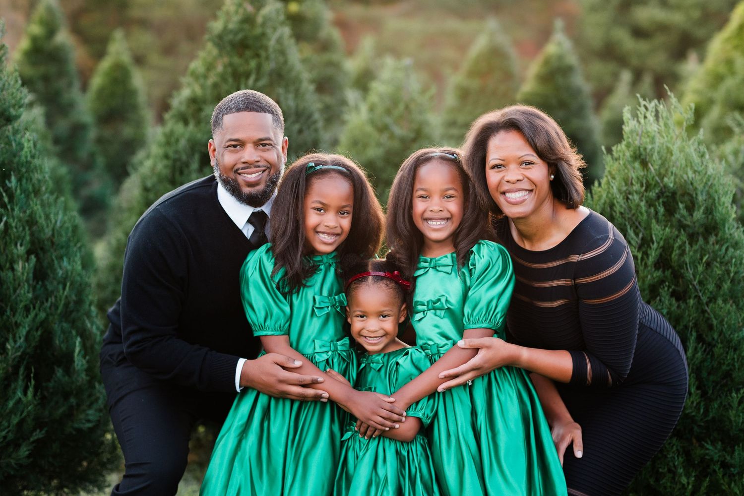 Family wearing coordinated green outfits poses together for outdoor portrait session.