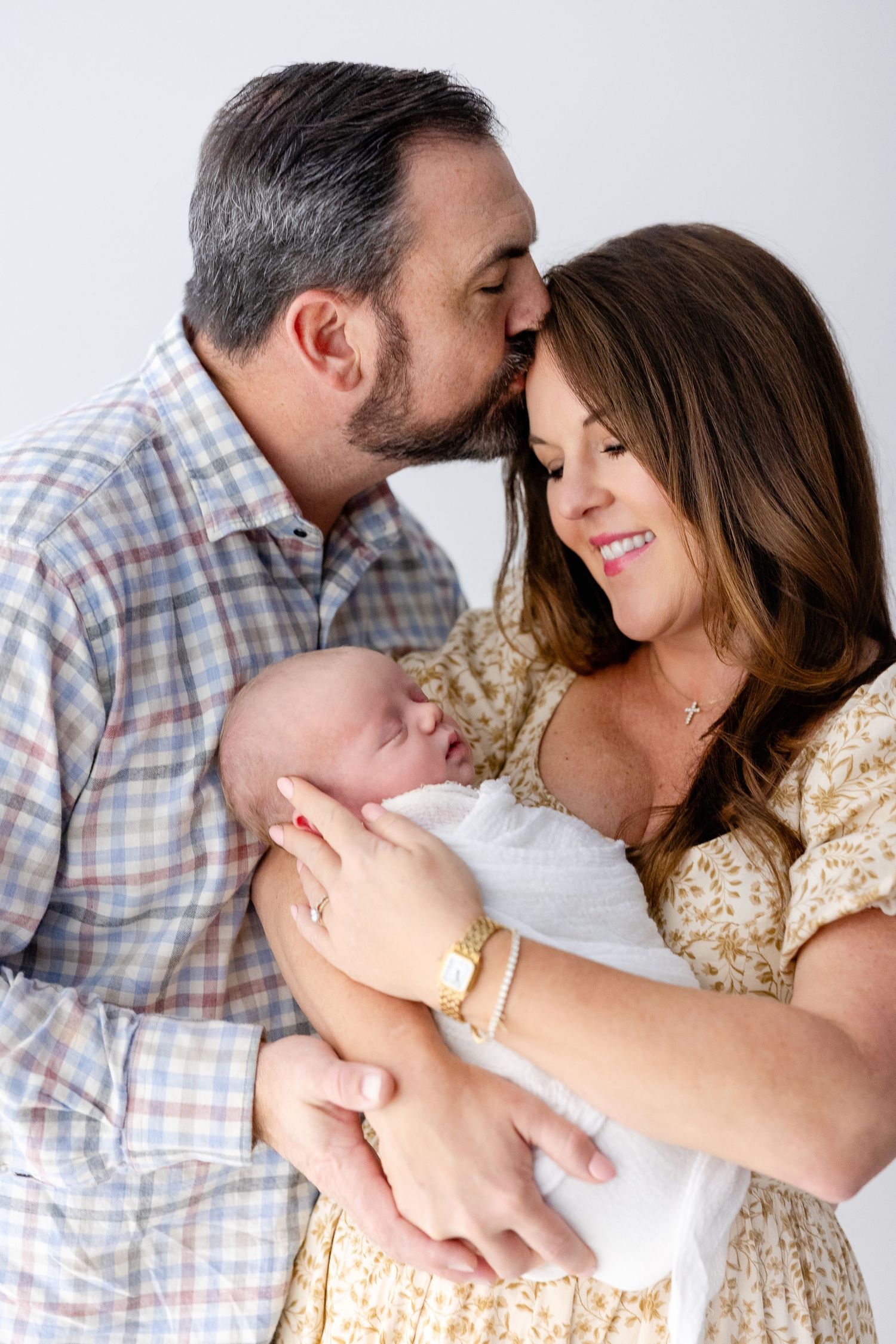 Intimate family moment captured in soft lighting against white background.