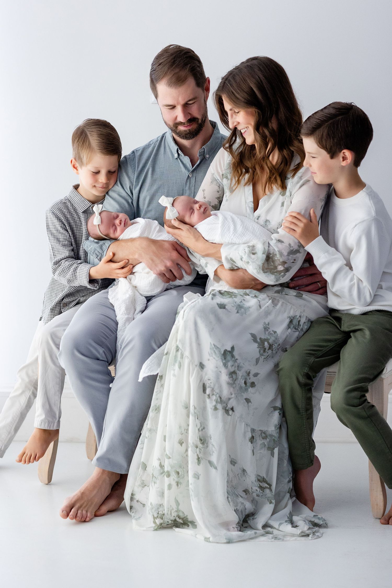 Family wearing coordinated gray and white outfits sits together on white backdrop in casual studio portraits.