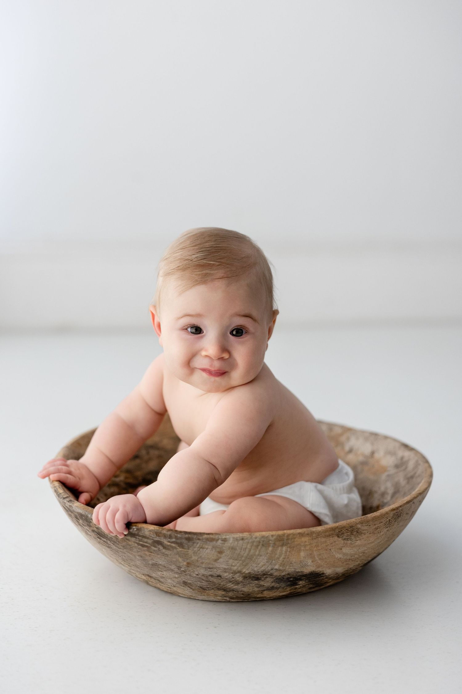 Baby posing in rustic wooden bowl against white background with adorable expressions.