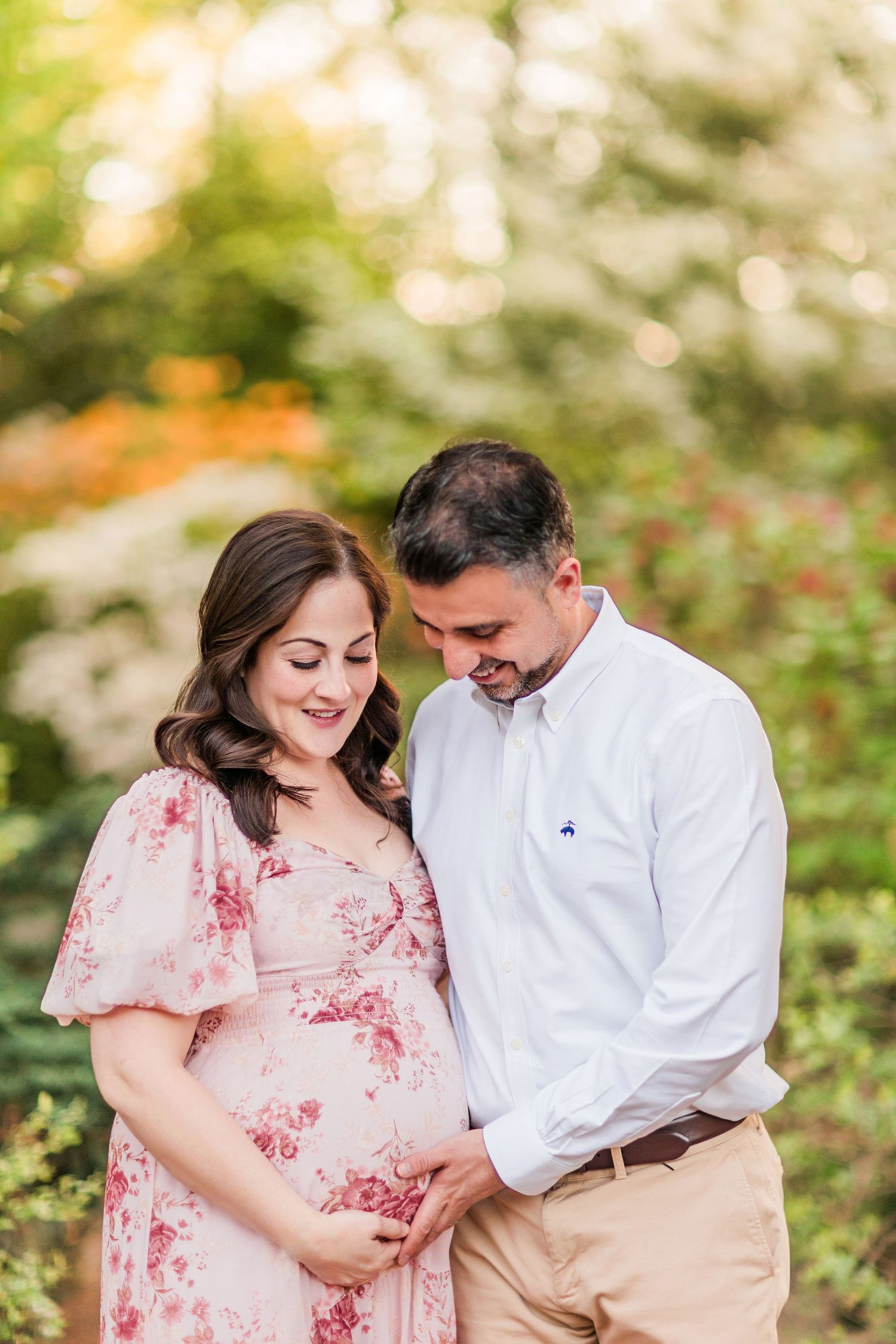 A couple shares intimate moments in a garden setting wearing a pink floral dress and white shirt with khaki pants.