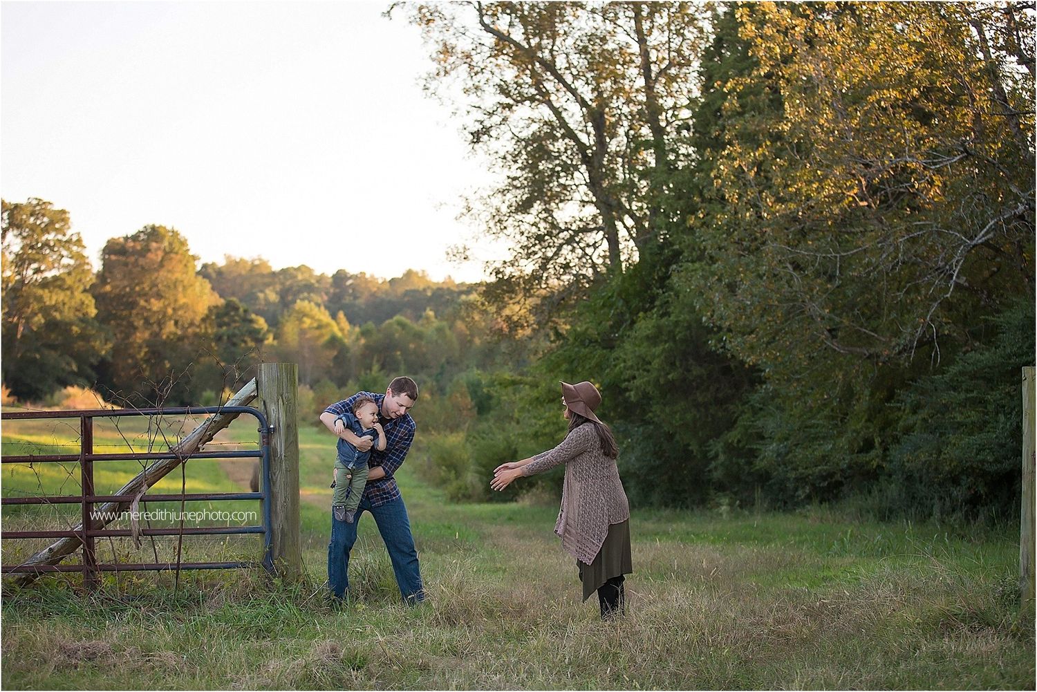 Family walking together through a scenic field at sunset with wooden fence in background.