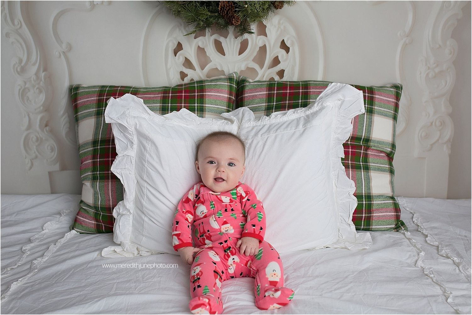 Festive holiday bedroom decor with plaid pillows, white bedding, and a wreath hanging on the wall.