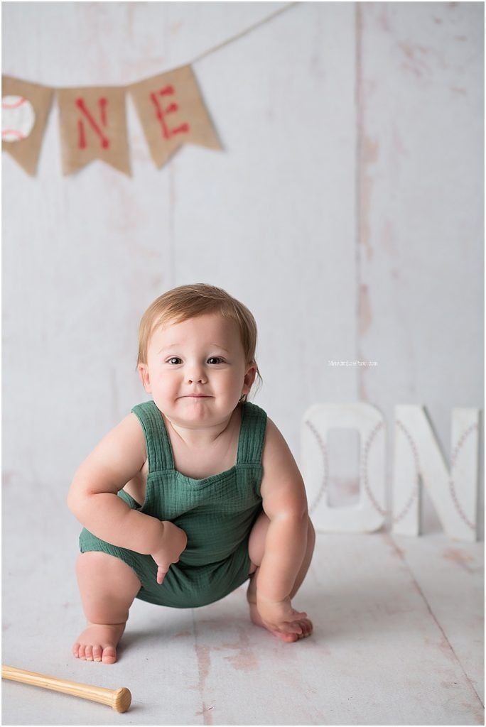 Baby in green romper crouches under ONE banner during photo session.