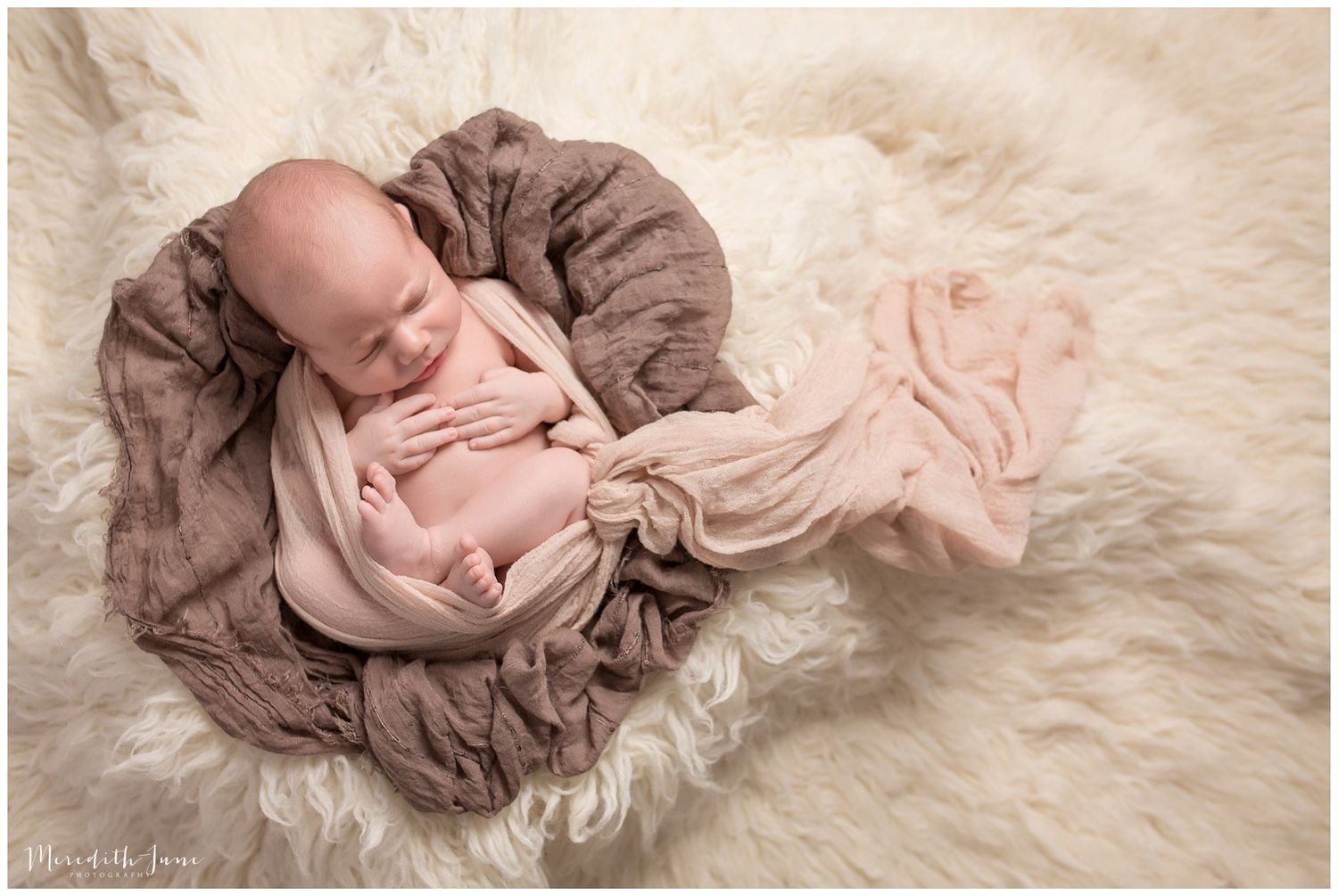 Newborn baby wrapped in soft brown fabric lying on white fluffy rug in artistic photography poses.