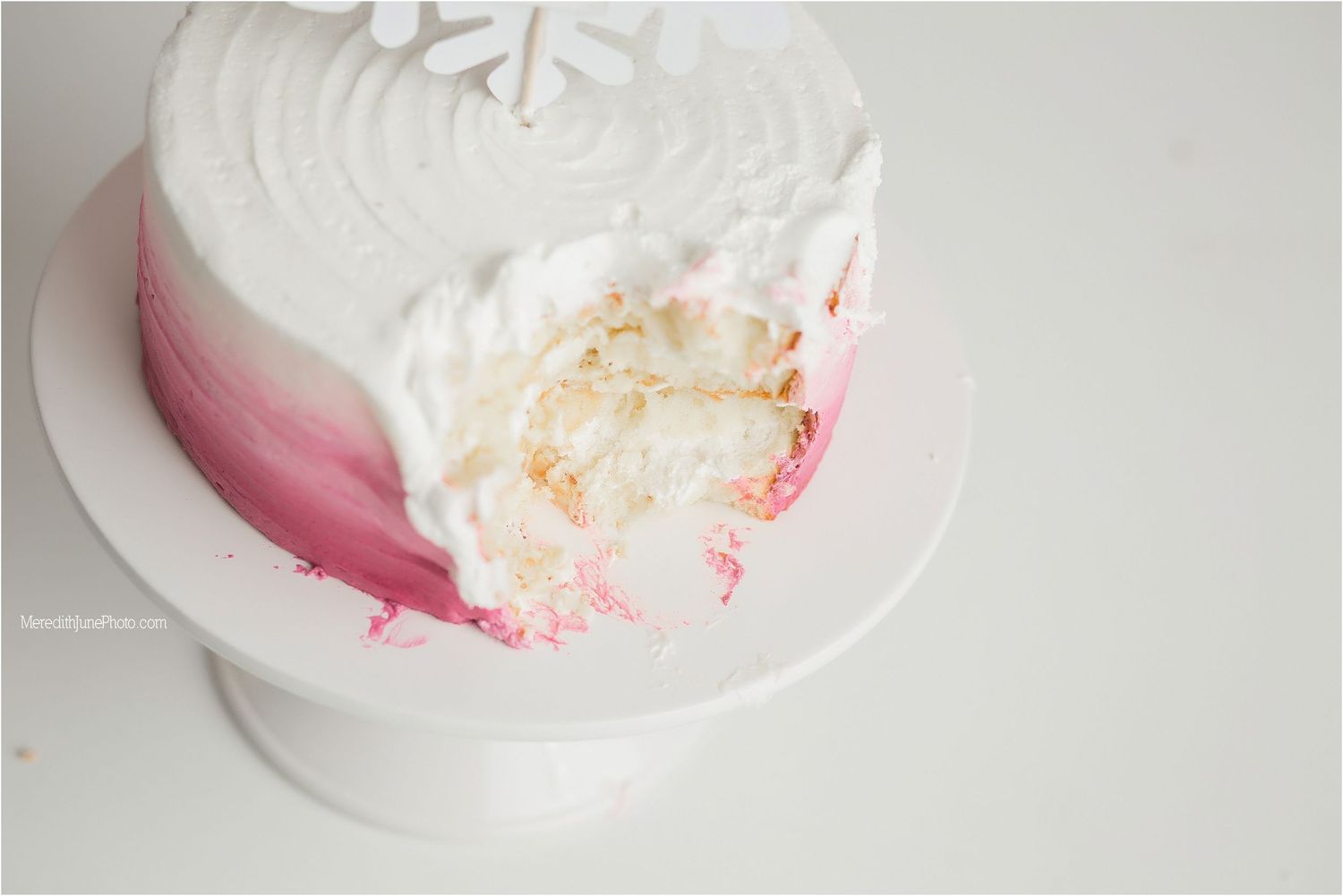 Close-up of white and pink ombre cake with smashed section revealing layers inside.