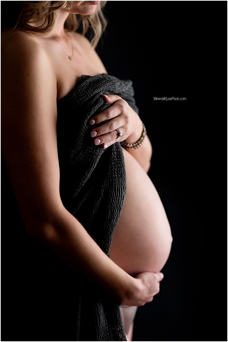 Intimate maternity portrait showing pregnant belly draped in black fabric against dark background.