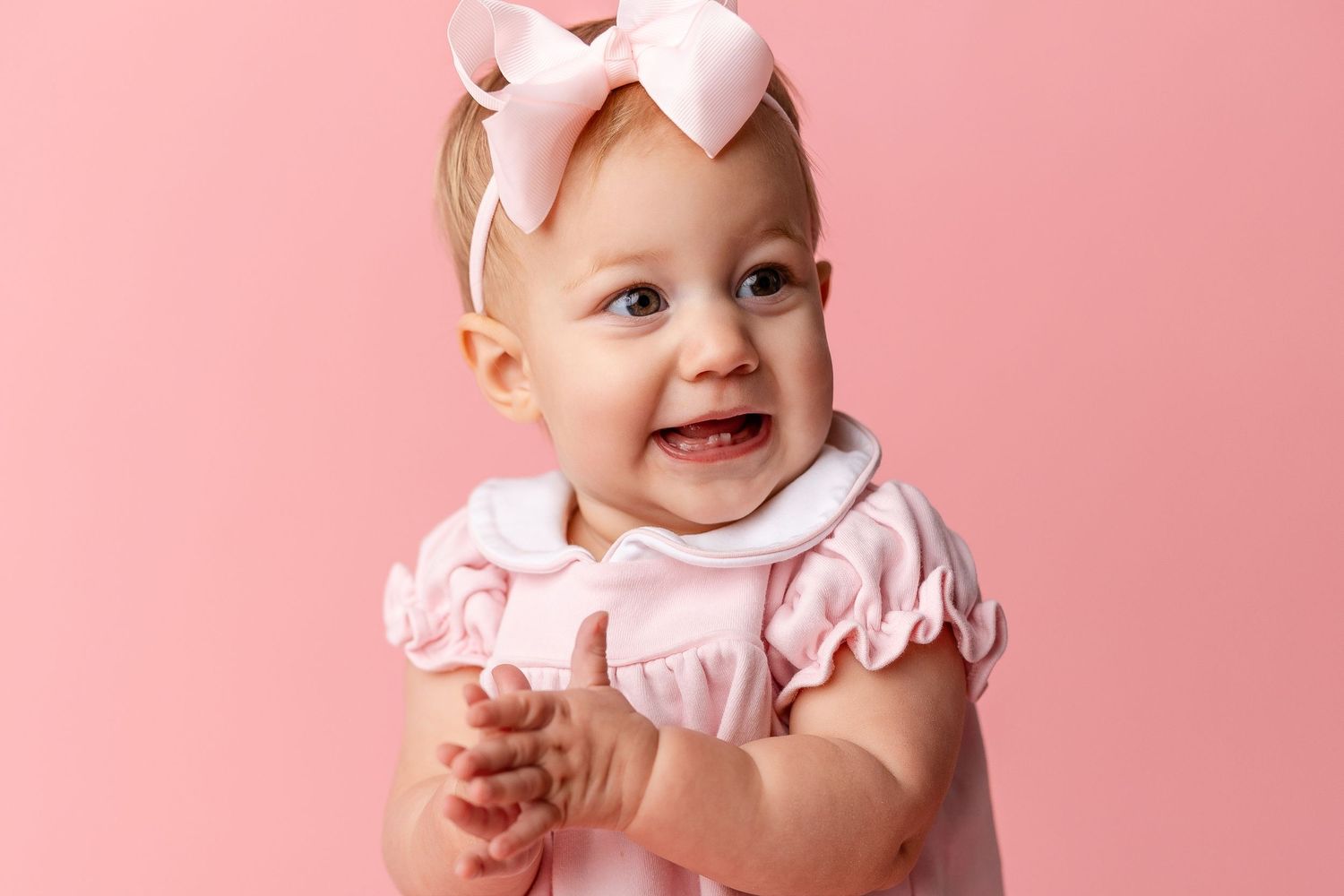 A baby in a pink dress smiles and poses in a series of connected photos against a pink background.