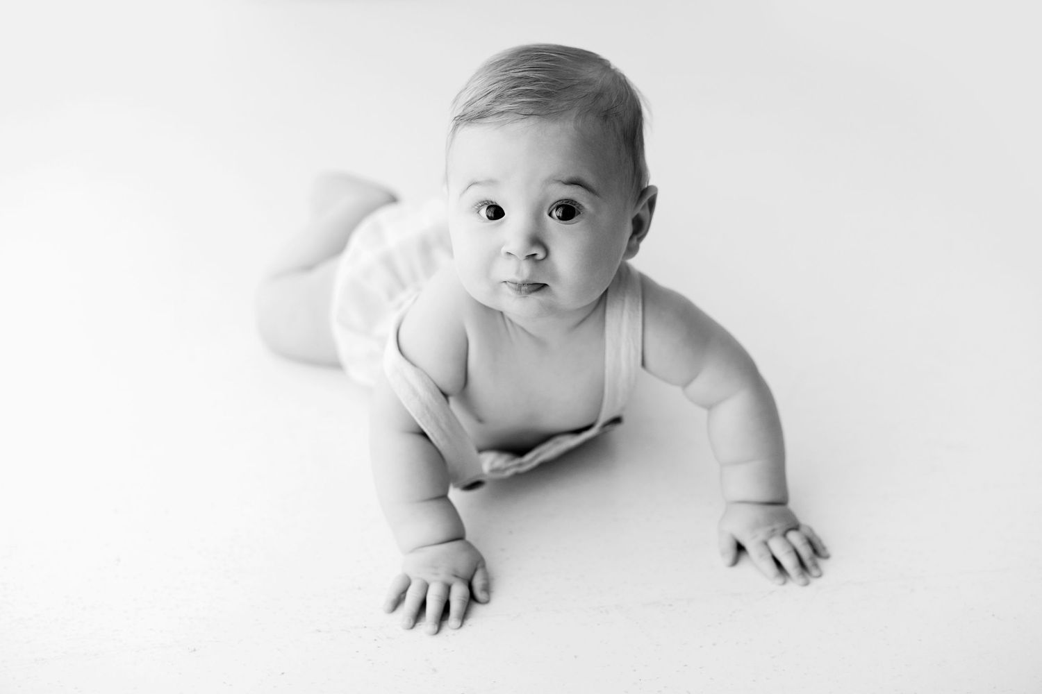 Black and white photo series showing a baby lying on their tummy in different poses on a white background.