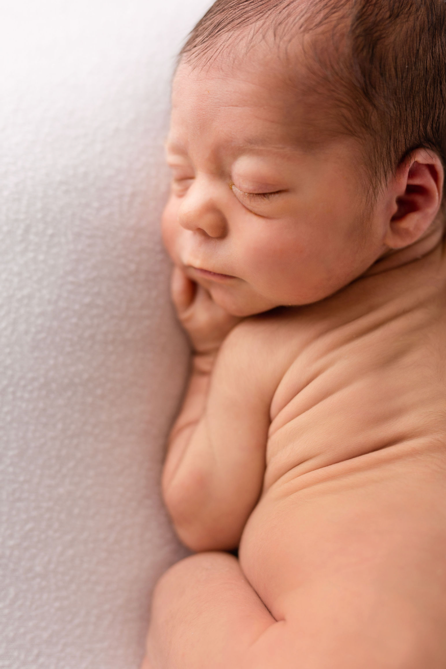 A sleeping newborn baby lies peacefully on a soft white blanket in a series of gentle poses.