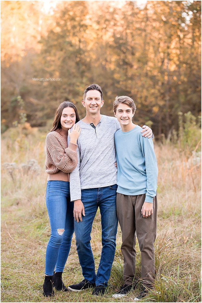 A family poses together in casual clothing against a golden autumn field at sunset.