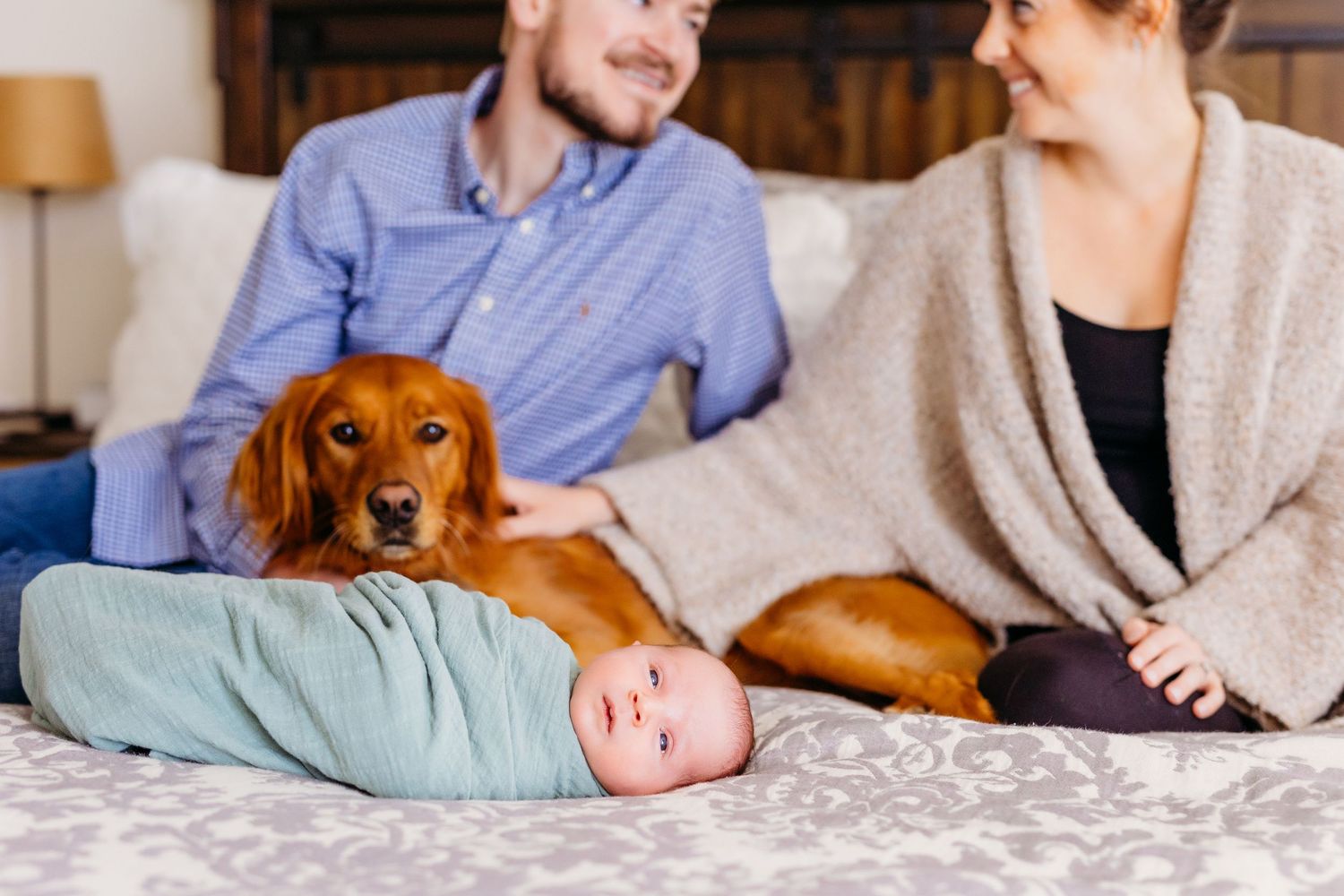 Golden retriever watches over sleeping baby in cozy home setting with warm lighting.