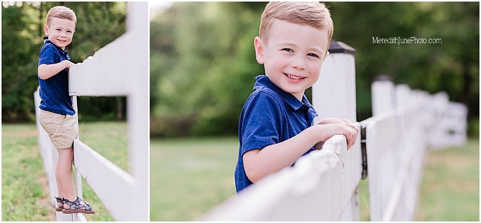 Young child in navy polo shirt and khaki shorts leaning playfully against white fence on sunny day.