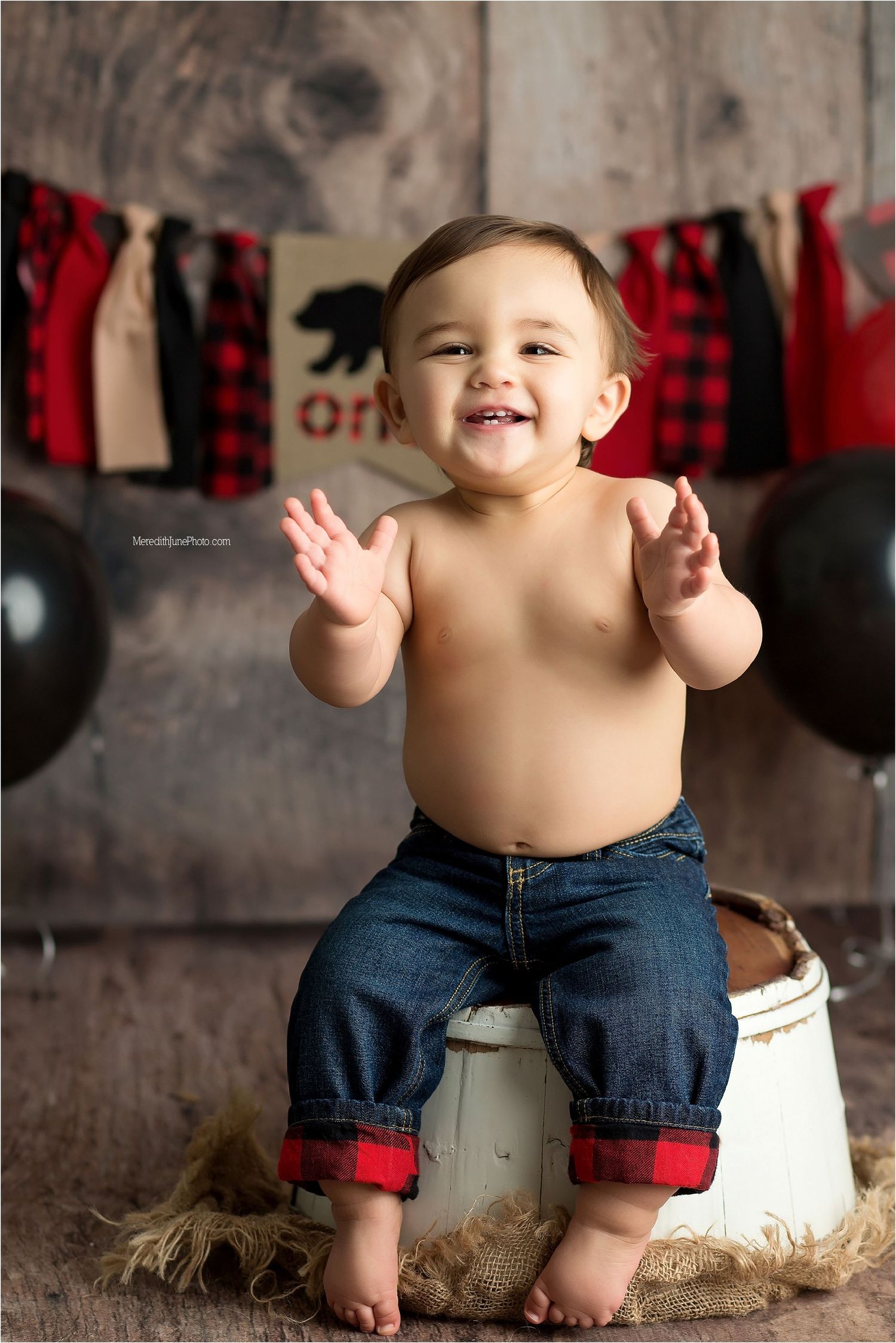 A small child in denim shorts sits on a rustic surface with buffalo plaid decor in the background.