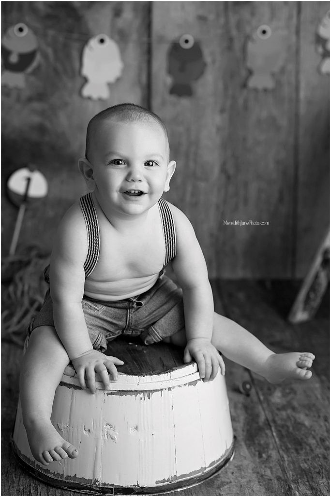 Black and white portraits of baby sitting on vintage white barrel during cake smash session.