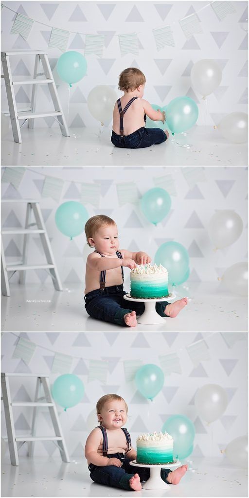 Baby in navy suspenders enjoys first birthday cake smash photoshoot with teal balloons and ombre cake against geometric backdrop.