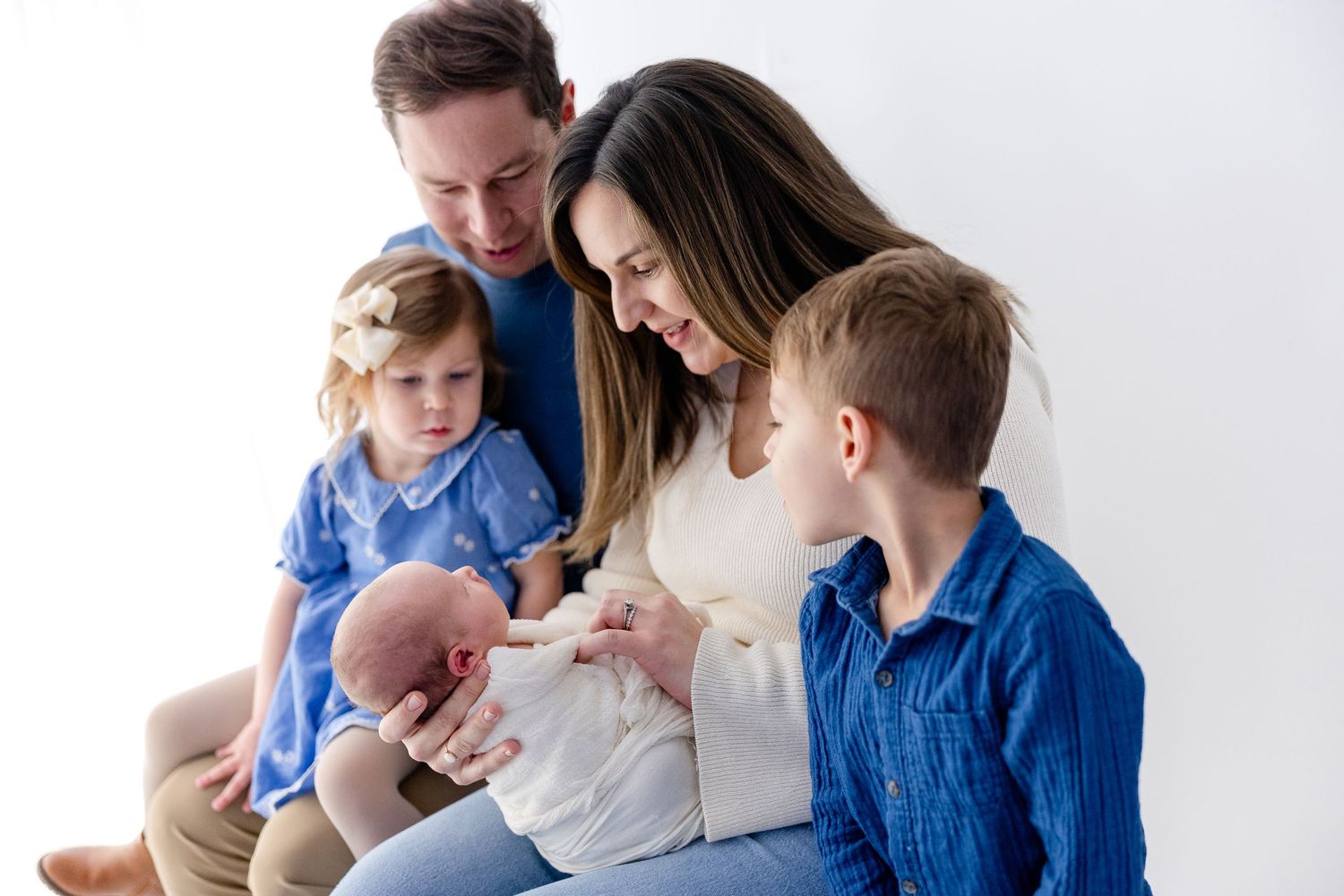 A family in coordinating blue outfits sits together on a couch during a casual photo session.