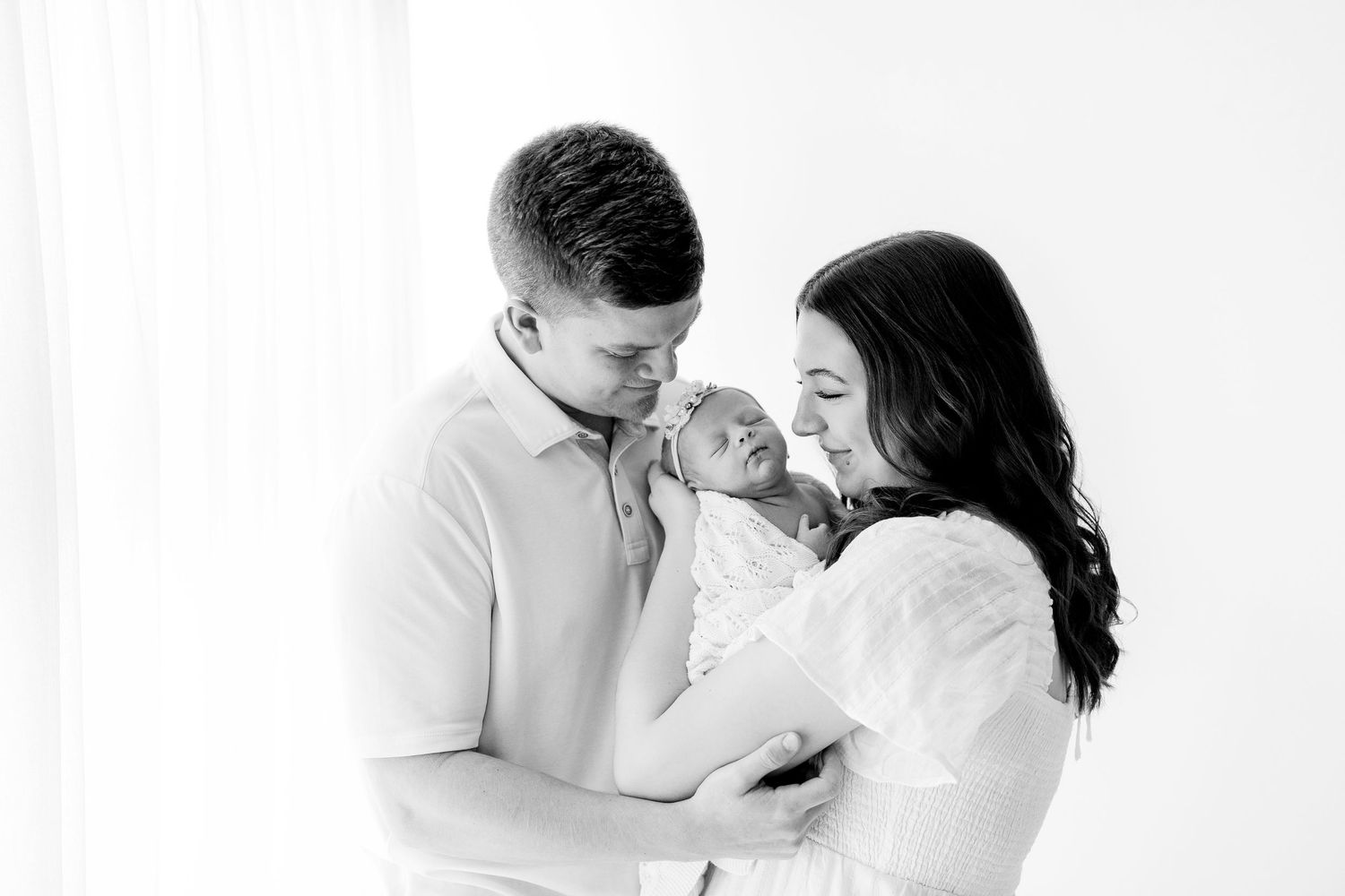 A series of black and white photos showing tender moments between a couple embracing and holding their newborn baby.