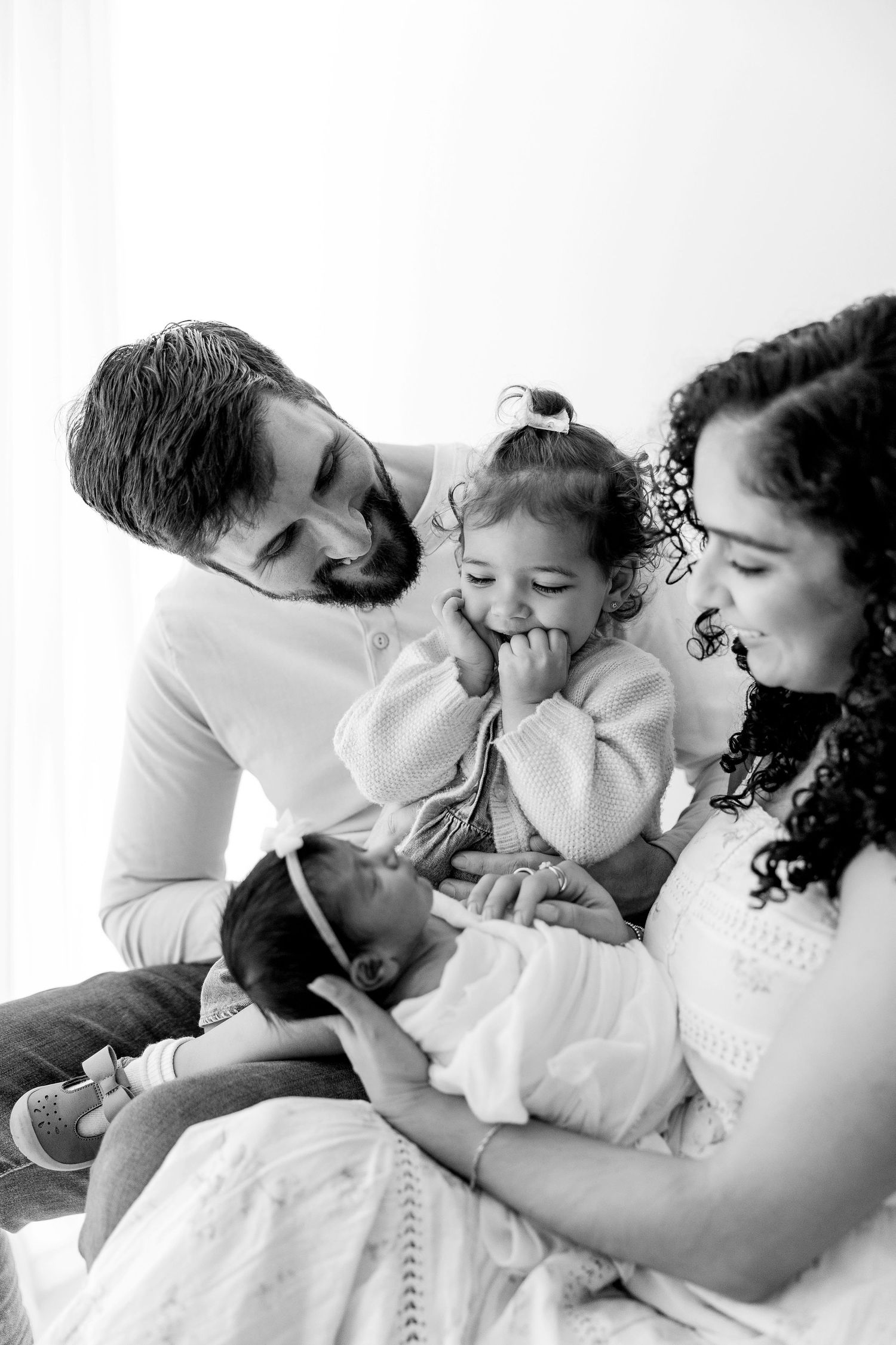 A tender black and white photo series showing intimate family moments as they cuddle together on white bedding.