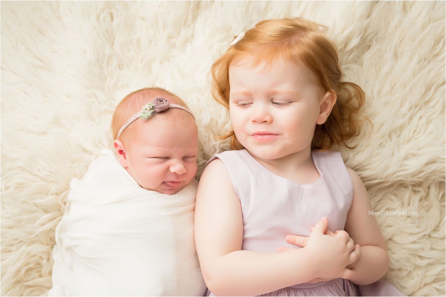Two children resting together on cream-colored blanket in gentle natural light.